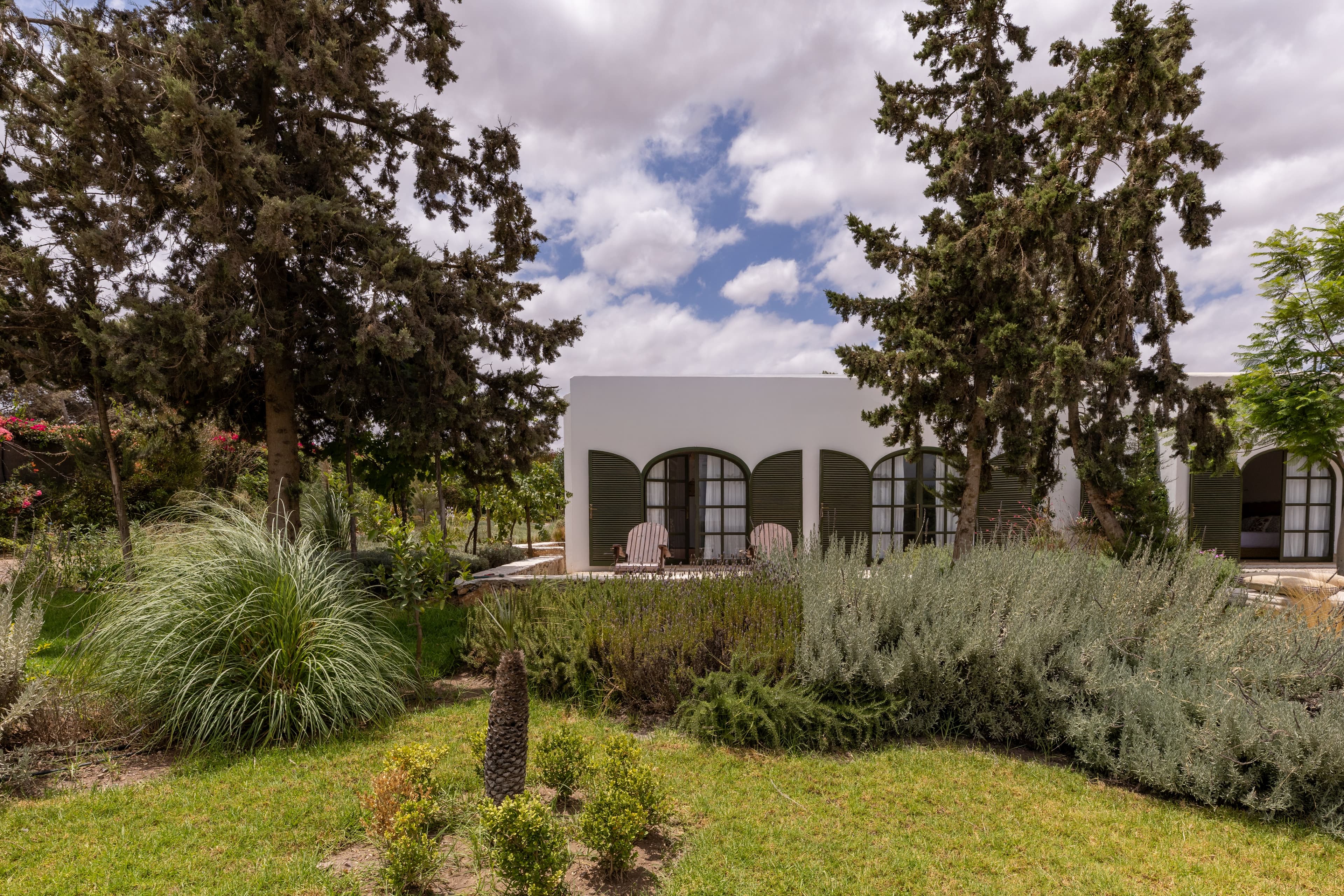 Les arches vertes de la bâtisse blanche entre cyprès, lavandes et graminées du jardin