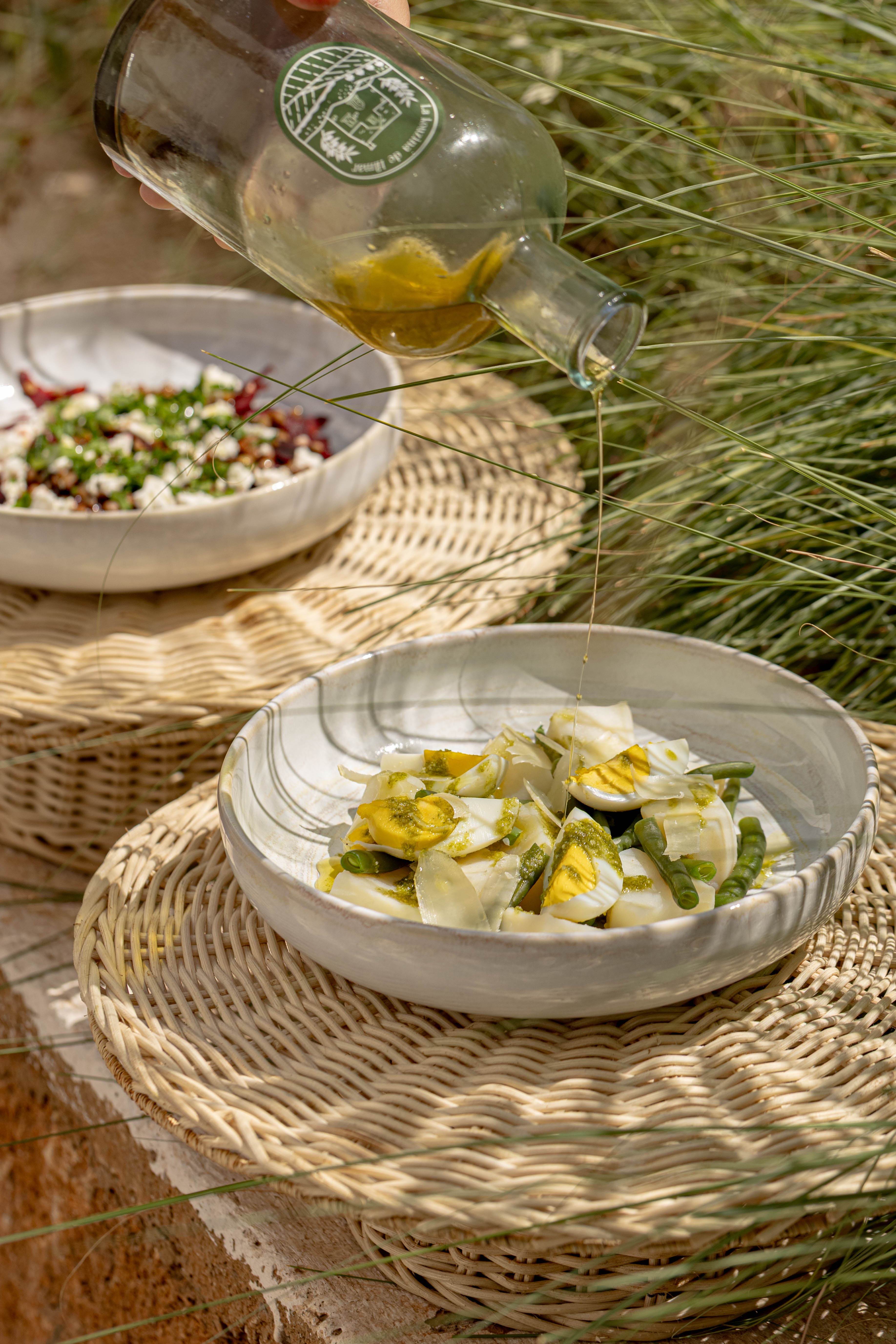 Huile d'olive du domaine versée en filet sur une salade d'œufs et haricots verts du potager